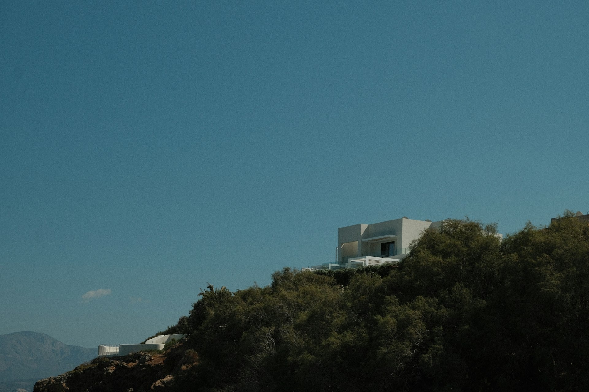 White modern villa on a green hillside beneath a clear blue sky